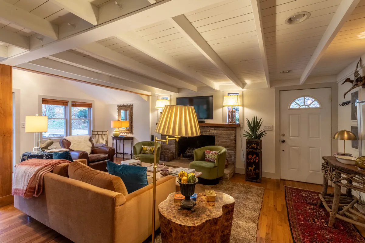 A welcoming living room featuring a plush sofa and armchairs arranged around a stone fireplace, with a Smart HDTV perched above the mantle. Warm lighting and tasteful decor create a cozy, inviting atmosphere ideal for relaxing or socializing.