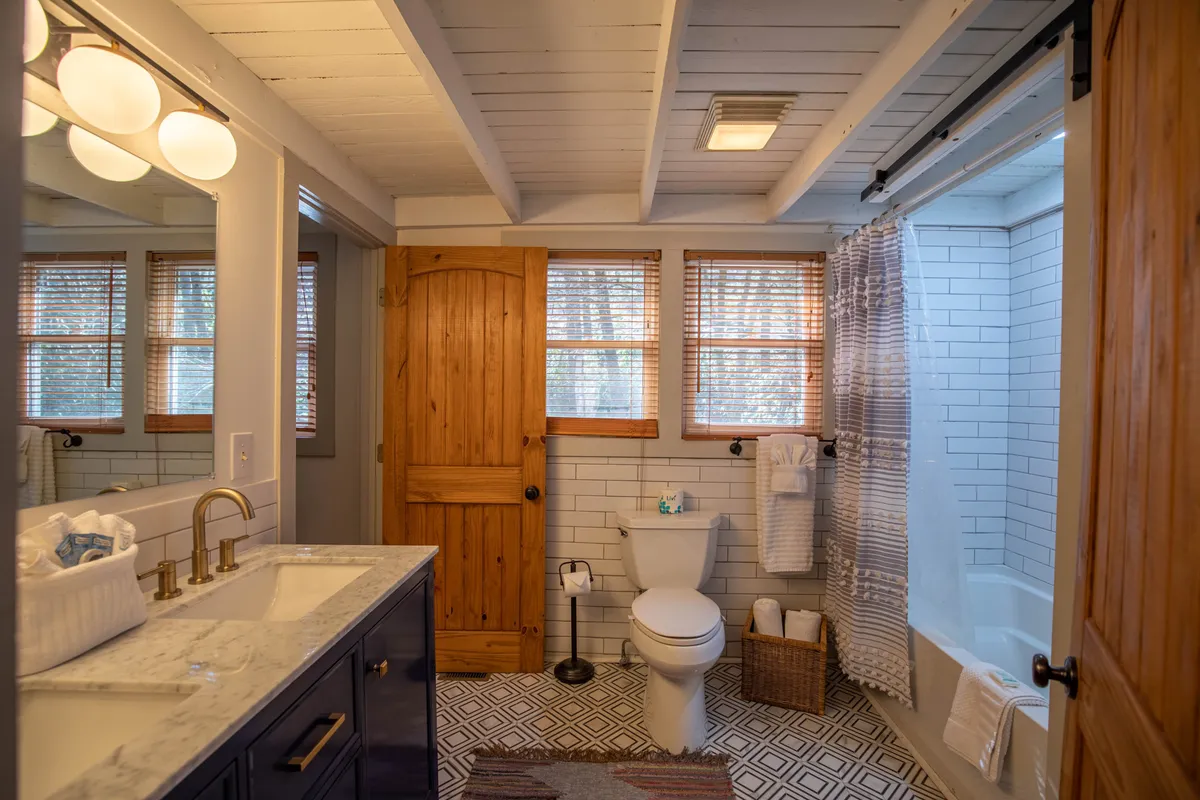 A calming bathroom scene featuring a modern vanity with a sink, a wooden door, a bathtub, and a toilet. The soft lighting and clean design convey relaxation and privacy.